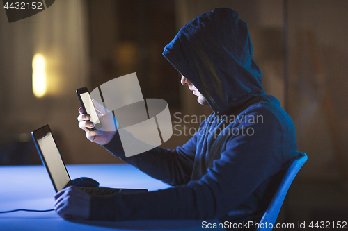 Image of hacker with laptop and smartphone in dark room