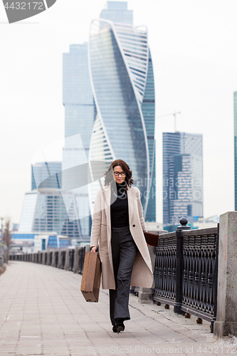 Image of Beautiful business woman in a long light coat comes with a case 