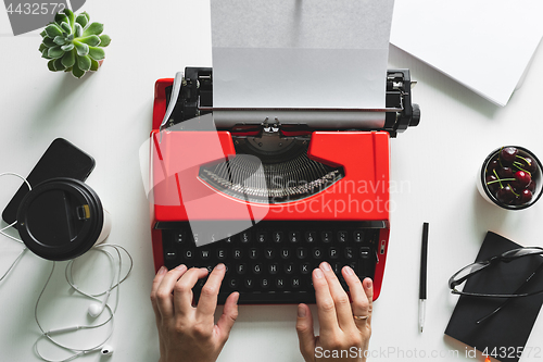 Image of Woman hand working with bright red vintage typewriter