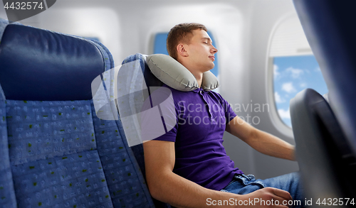 Image of young man sleeping in plane with travel pillow