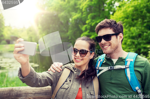 Image of couple with backpacks taking selfie by smartphone