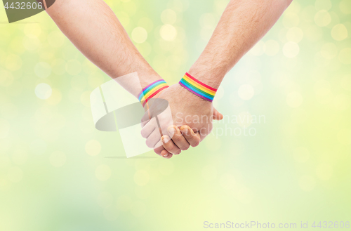 Image of hands of couple with gay pride rainbow wristbands