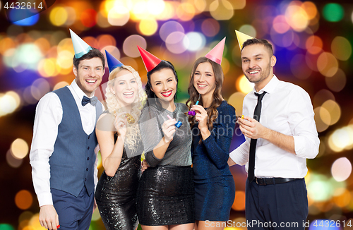Image of happy friends with party blowers over lights