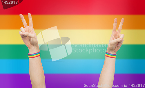 Image of hands with gay pride rainbow wristbands make peace