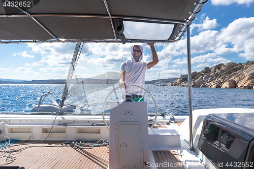 Image of Attractive male skipper navigating the fancy catamaran sailboat on sunny summer day on calm blue sea water.