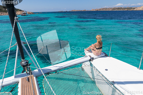 Image of Woman relaxing on a summer sailing cruise, sitting on a luxury catamaran in picture perfect turquoise blue lagoon near Spargi island in Maddalena Archipelago, Sardinia, Italy.