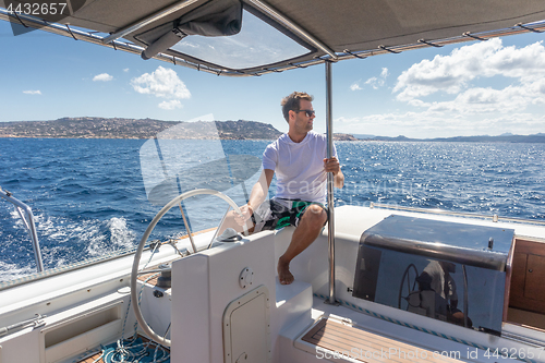 Image of Attractive male skipper navigating the fancy catamaran sailboat on sunny summer day on calm blue sea water.