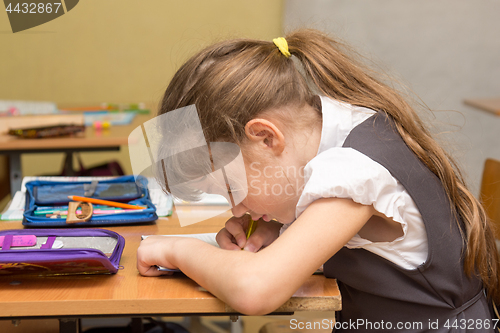 Image of A schoolgirl with a wrong posture at the lesson writes in a notebook