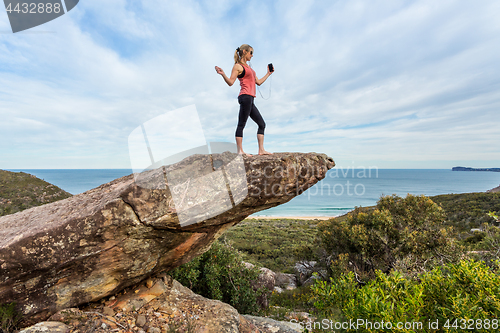 Image of Woman listening to music or a playlist high up on a balancing rock on mountain edge.