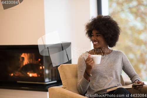 Image of black woman reading book  in front of fireplace