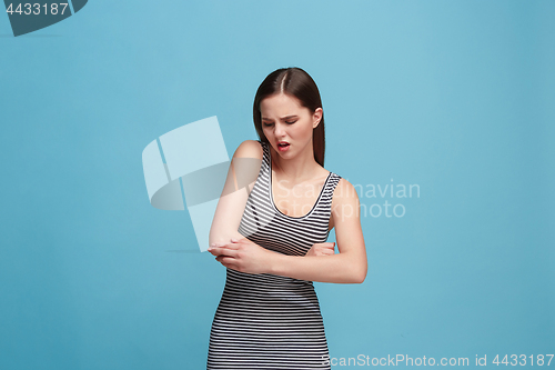 Image of The elbow ache. The sad woman with elbow ache or pain on a blue studio background.