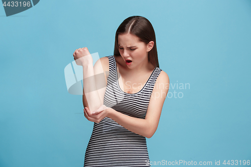 Image of The elbow ache. The sad woman with elbow ache or pain on a blue studio background.