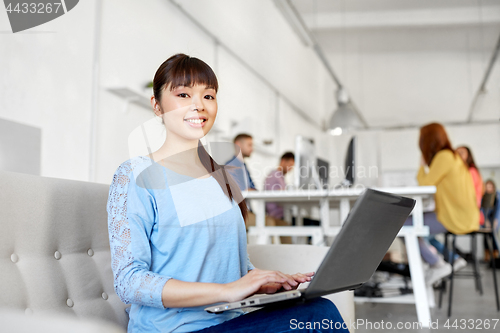 Image of happy asian woman with laptop working at office