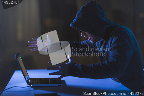 Image of angry hacker with laptop computer in dark room