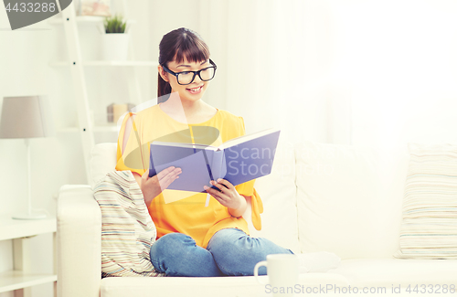 Image of smiling young asian woman reading book at home