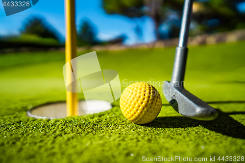 Image of Mini Golf yellow ball with a bat near the hole at sunset