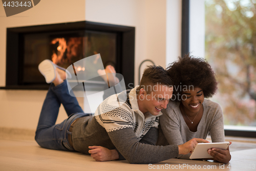 Image of multiethnic couple using tablet computer on the floor