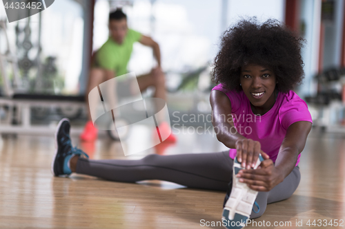 Image of woman in a gym stretching and warming up man in background worki