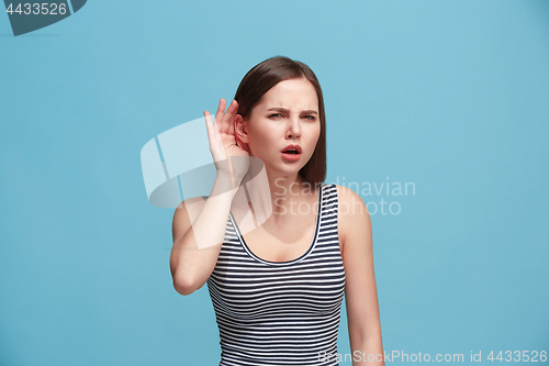 Image of The young woman is listening something on the blue background.