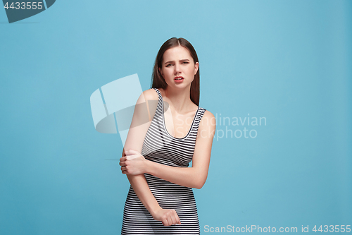 Image of The elbow ache. The sad woman with elbow ache or pain on a blue studio background.