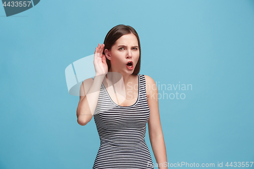 Image of The young woman is listening something on the blue background.