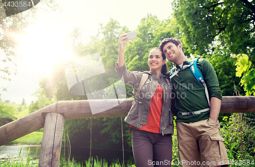 Image of couple with backpacks taking selfie by smartphone