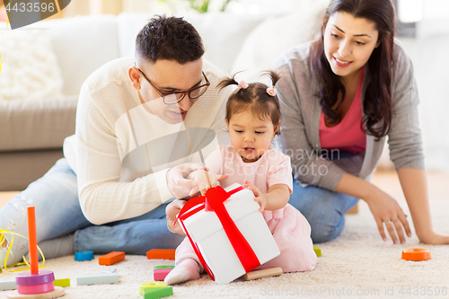 Image of baby girl with birthday gift and parents at home 