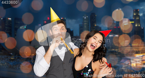 Image of happy couple with party blowers having fun