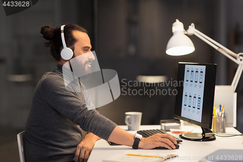 Image of creative man in headphones working at night office