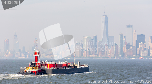 Image of Freight tug pushing cargo ship to the port in New York City and Lower Manhattan skyscarpers skyline in background.