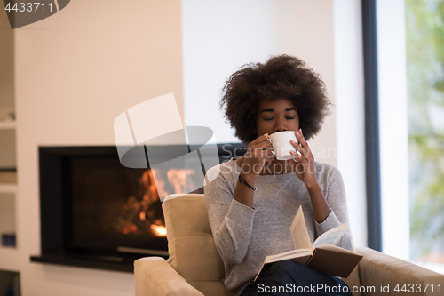 Image of black woman reading book  in front of fireplace