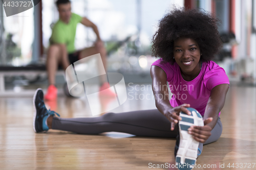 Image of woman in a gym stretching and warming up man in background worki