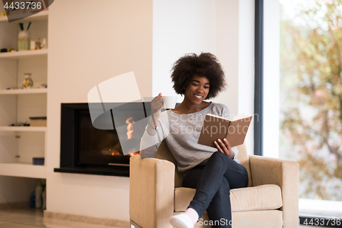 Image of black woman reading book  in front of fireplace