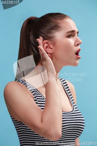 Image of The young woman is listening something on the blue background.