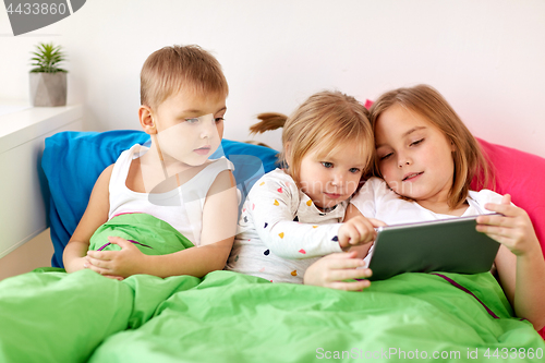 Image of little kids with tablet pc in bed at home