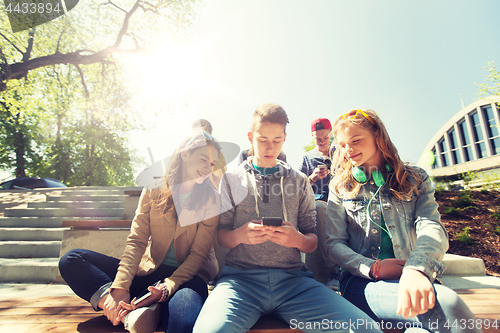 Image of happy teenage friends with smartphones outdoors