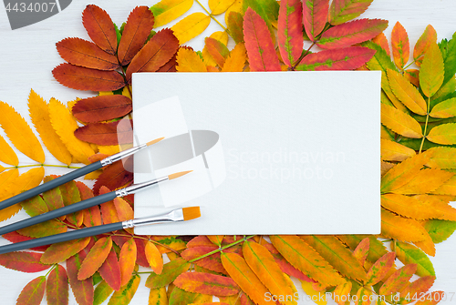 Image of Paintbrushes and white canvas on autumn leaves background