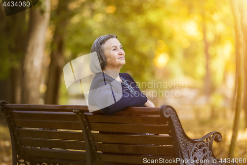 Image of Elderly woman sitting on a bench in autumn park