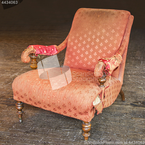 Image of Old tattered red armchair on a wooden parquet