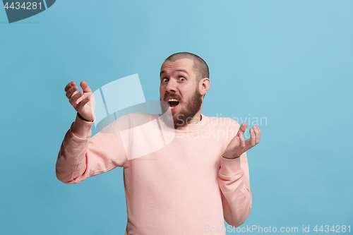 Image of Beautiful male half-length portrait isolated on blue studio backgroud. The young emotional surprised man