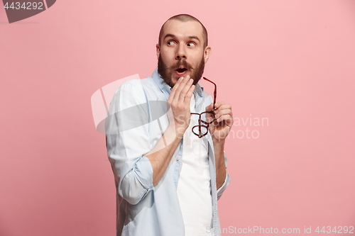 Image of The young man whispering a secret behind her hand over pink background