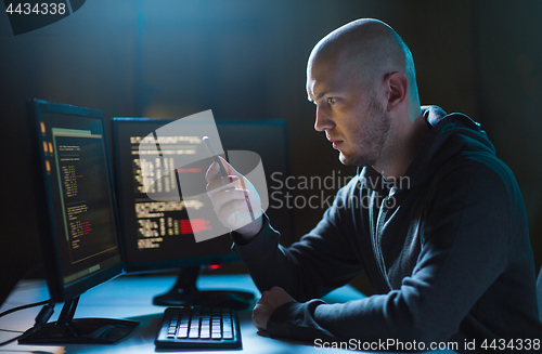 Image of hacker with smartphone and computers in dark room