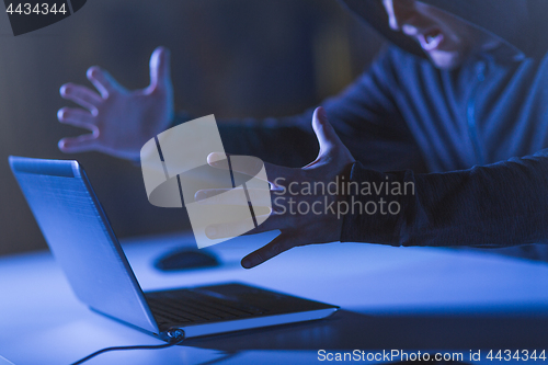 Image of angry hacker with laptop shouting in dark room