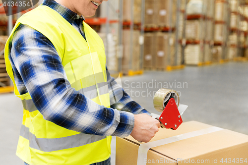 Image of warehouse worker packing parcel with scotch tape