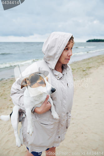 Image of Woman in jacket holding dog on beach