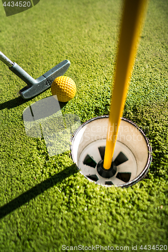 Image of Mini Golf yellow ball with a bat near the hole at sunset