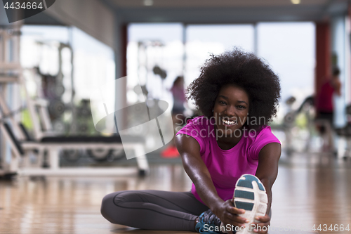 Image of woman in a gym stretching and warming up man in background worki