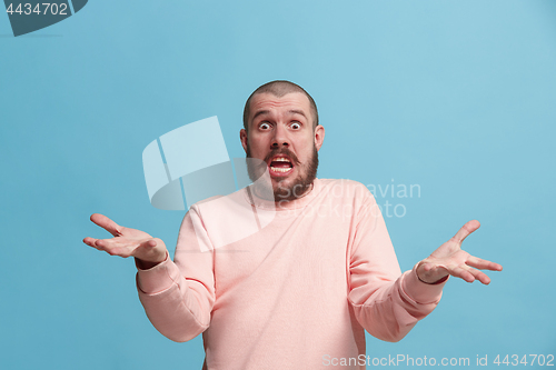 Image of Beautiful male half-length portrait isolated on blue studio backgroud. The young emotional surprised man