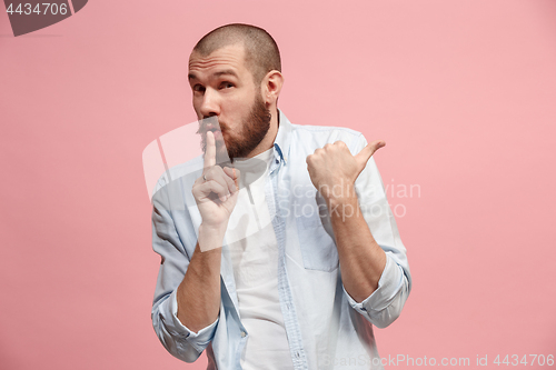 Image of The young man whispering a secret behind her hand over pink background