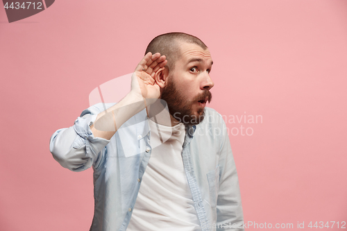 Image of The young man whispering a secret behind her hand over pink background